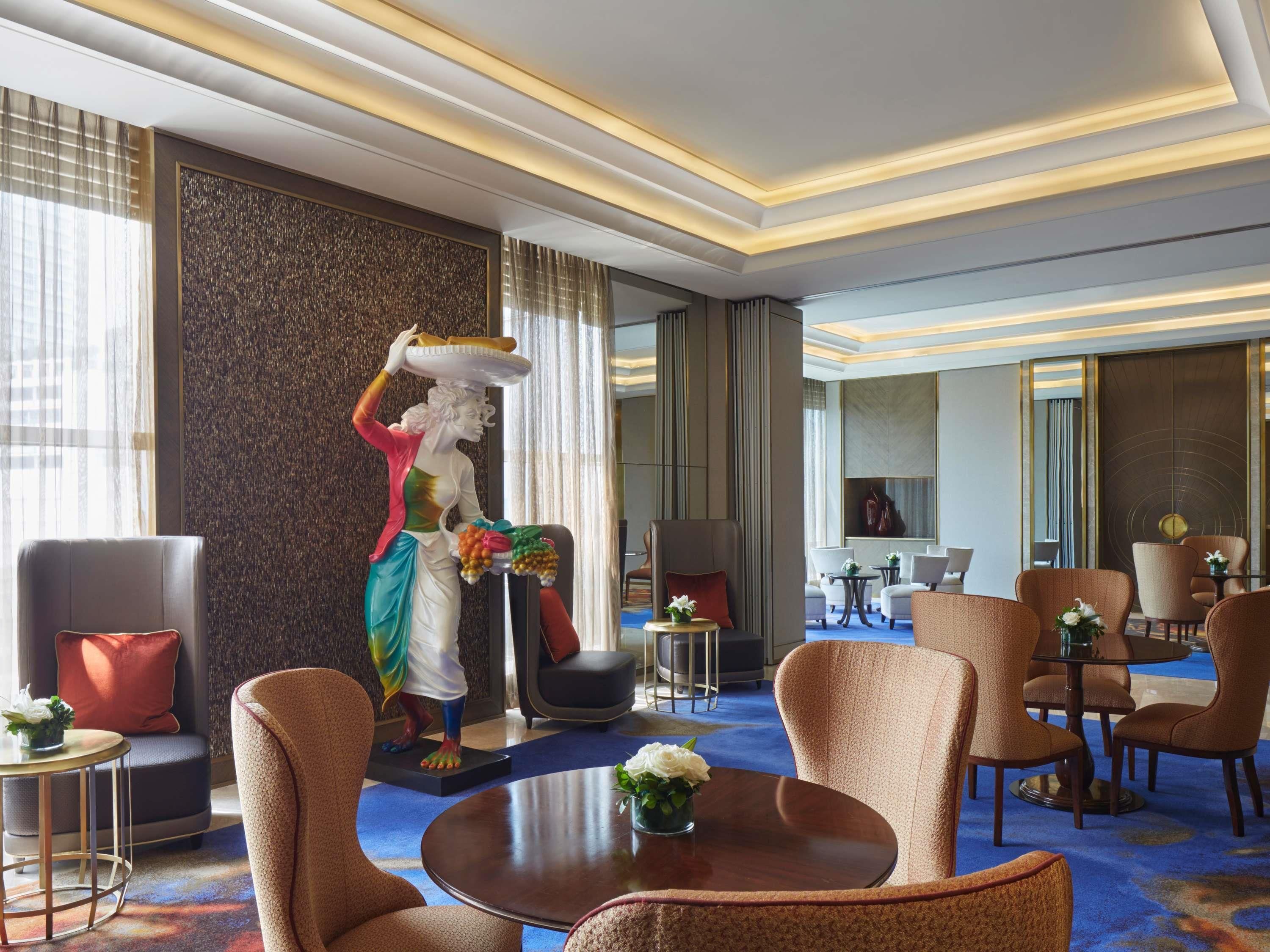 Een hotellobby met een standbeeld, zithoekjes en een groot raam.