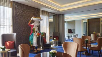 Een hotellobby met een standbeeld, zithoekjes en een groot raam.