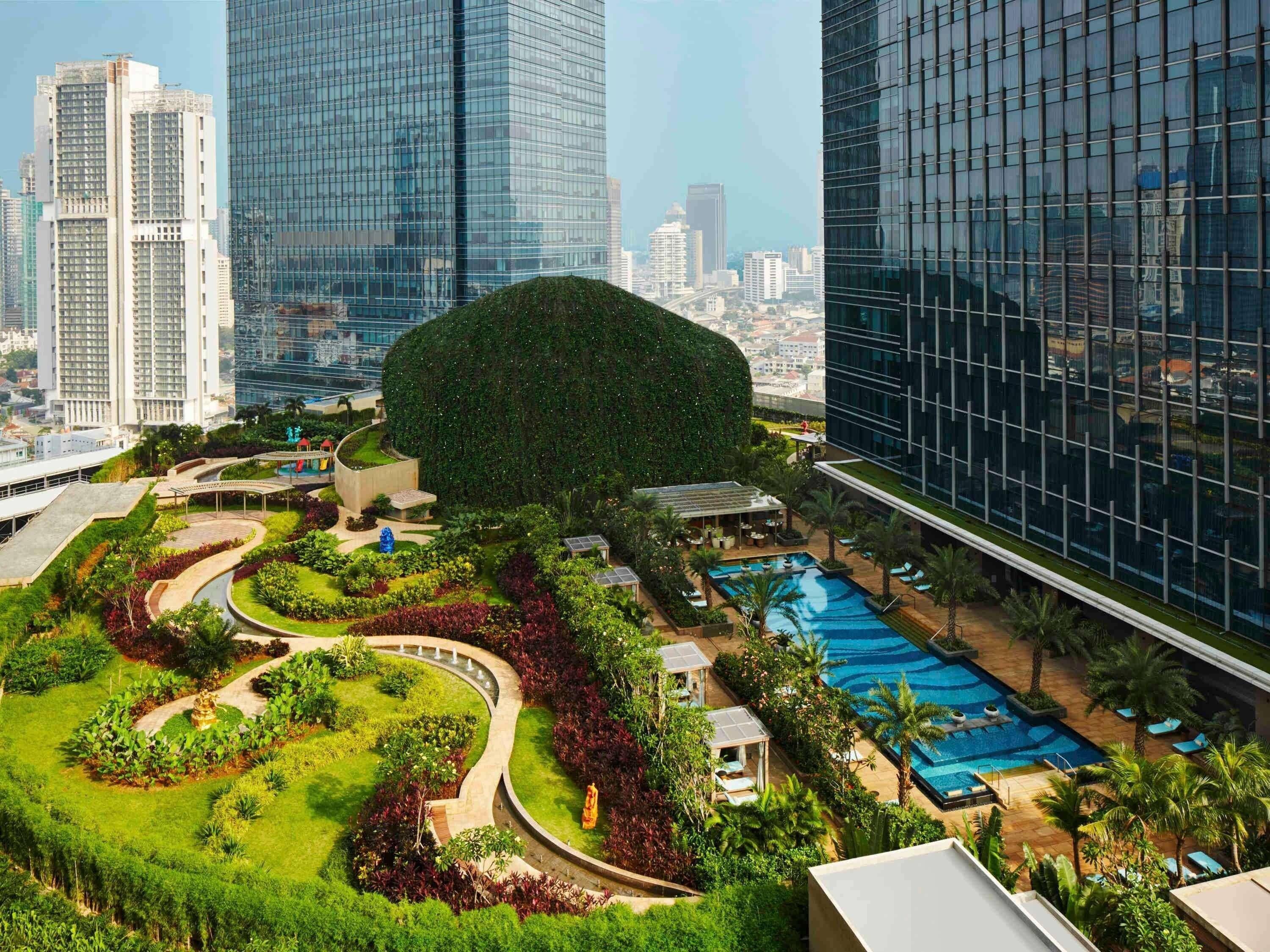 Un hotel moderno con jardín en la azotea, piscina y vistas de edificios altos aledaños.