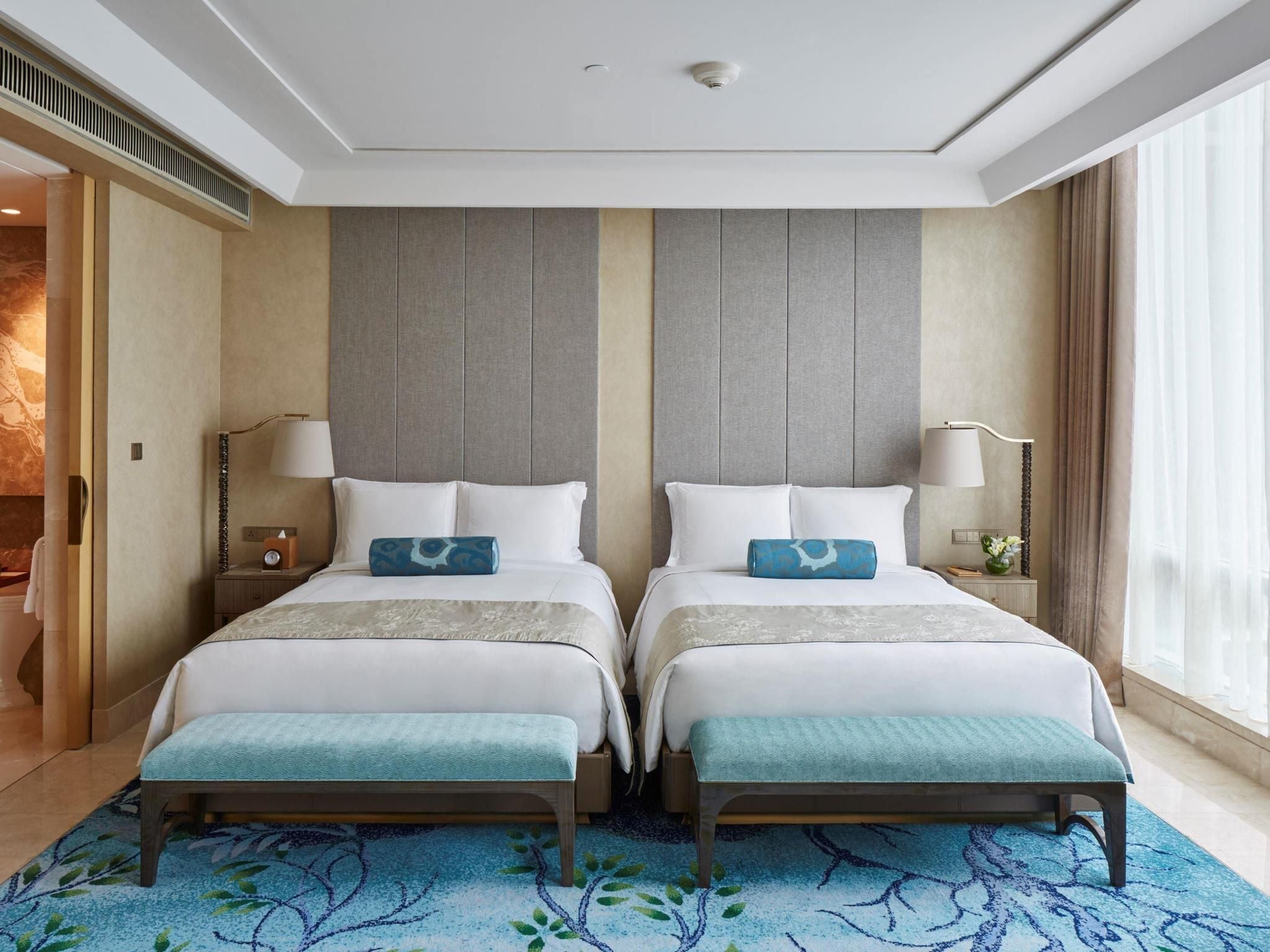 Habitación de hotel con dos camas, un tapete azul estampado y un ventanal con cortinas.