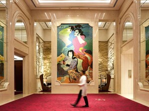 A hotel lobby with a large mural, a red carpet, and a modern chandelier.