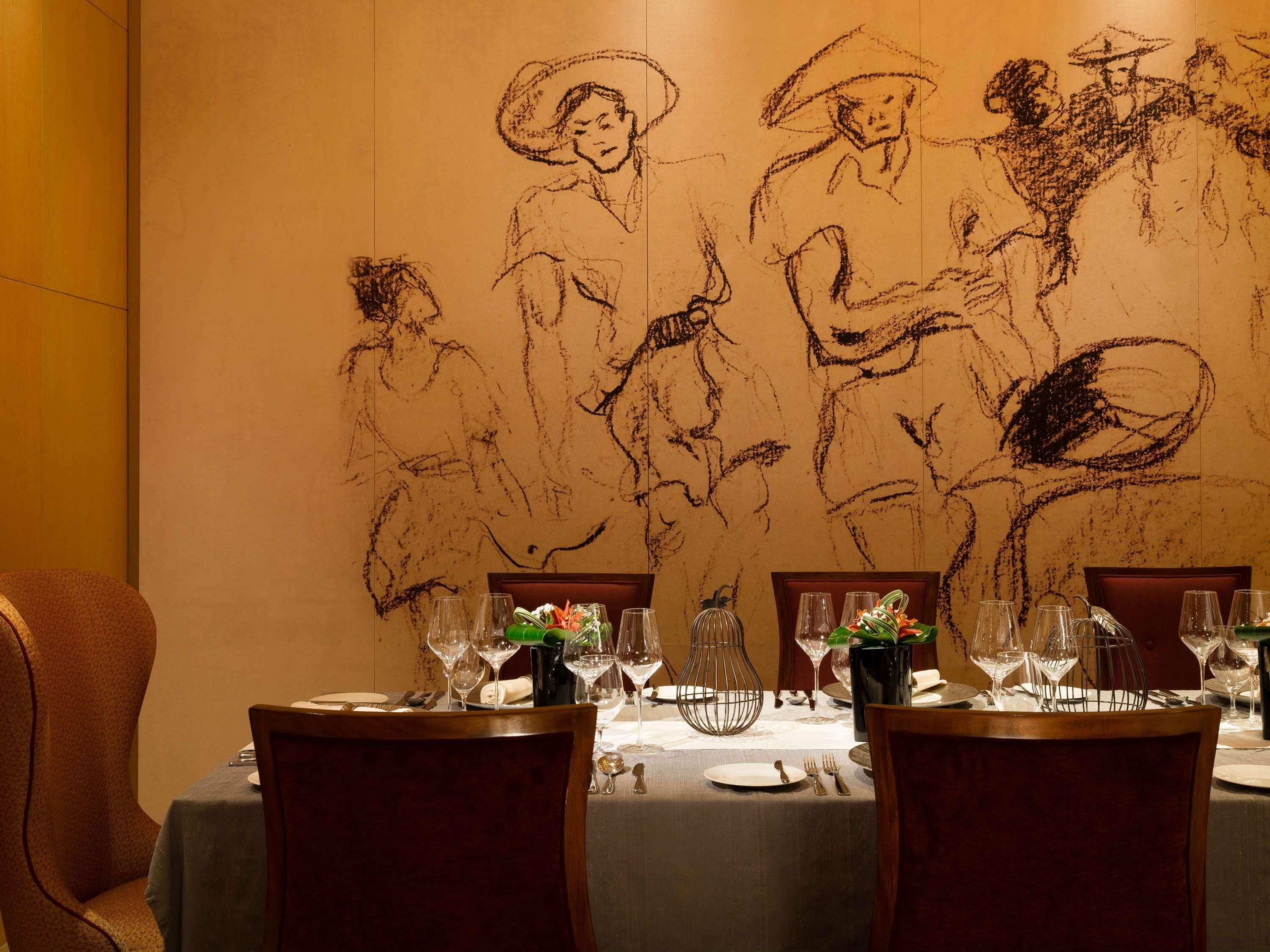 A dining table set with wine glasses, plates, and cutlery, with a large wall mural depicting people in historical attire.