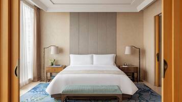 A hotel room with a large bed, two bedside tables, a bench, and a view of the outside through a window with curtains.