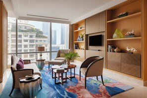 Una sala de estar moderna con un sofá, sillones, una mesa de centro y un televisor montado en la pared. Hay un ventanal grande que ofrece vistas de la ciudad.