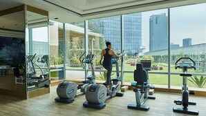 A modern gym with large windows, various exercise equipment, and a view of the cityscape. - Raffles Jakarta (Jakarta)
