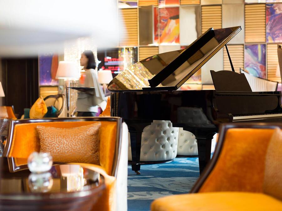 Un piano de cola en el vestíbulo de un hotel, con asientos lujosos y una alfombra estampada.