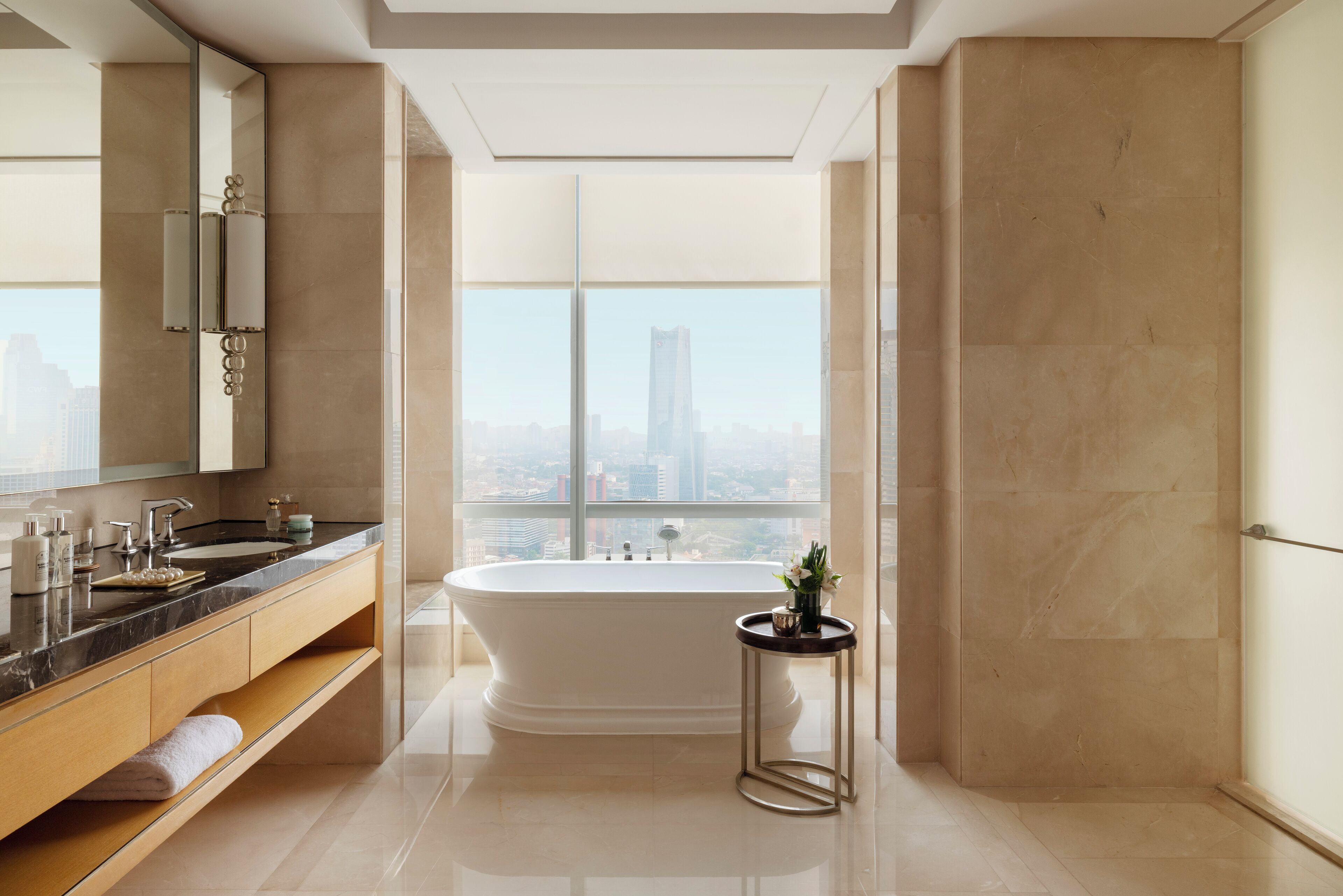 A modern bathroom with a freestanding bathtub, a large mirror, and a city view.