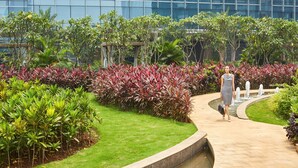 A landscaped garden with a curved pathway, lush greenery, and a modern building in the background. - Raffles Jakarta (Jakarta)