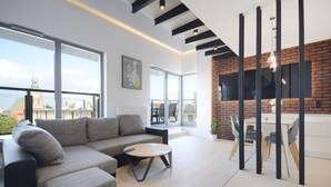 Un salon moderne avec un canapé d’angle, une table basse ronde et un coin repas agrémenté d’un mur en briques apparentes et d’un téléviseur à écran plat.