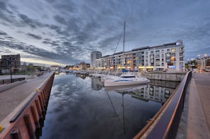 Ein Yachthafen mit vertäuten Booten, eine Uferpromenade und moderne Gebäude mit Balkonen.