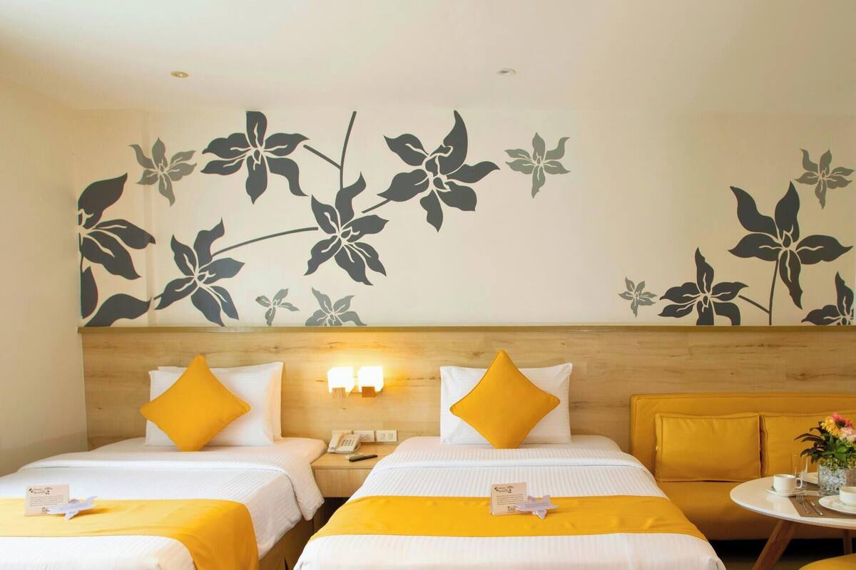 A hotel room with two beds, a sofa, a small table with a vase, and a wall with a floral mural.