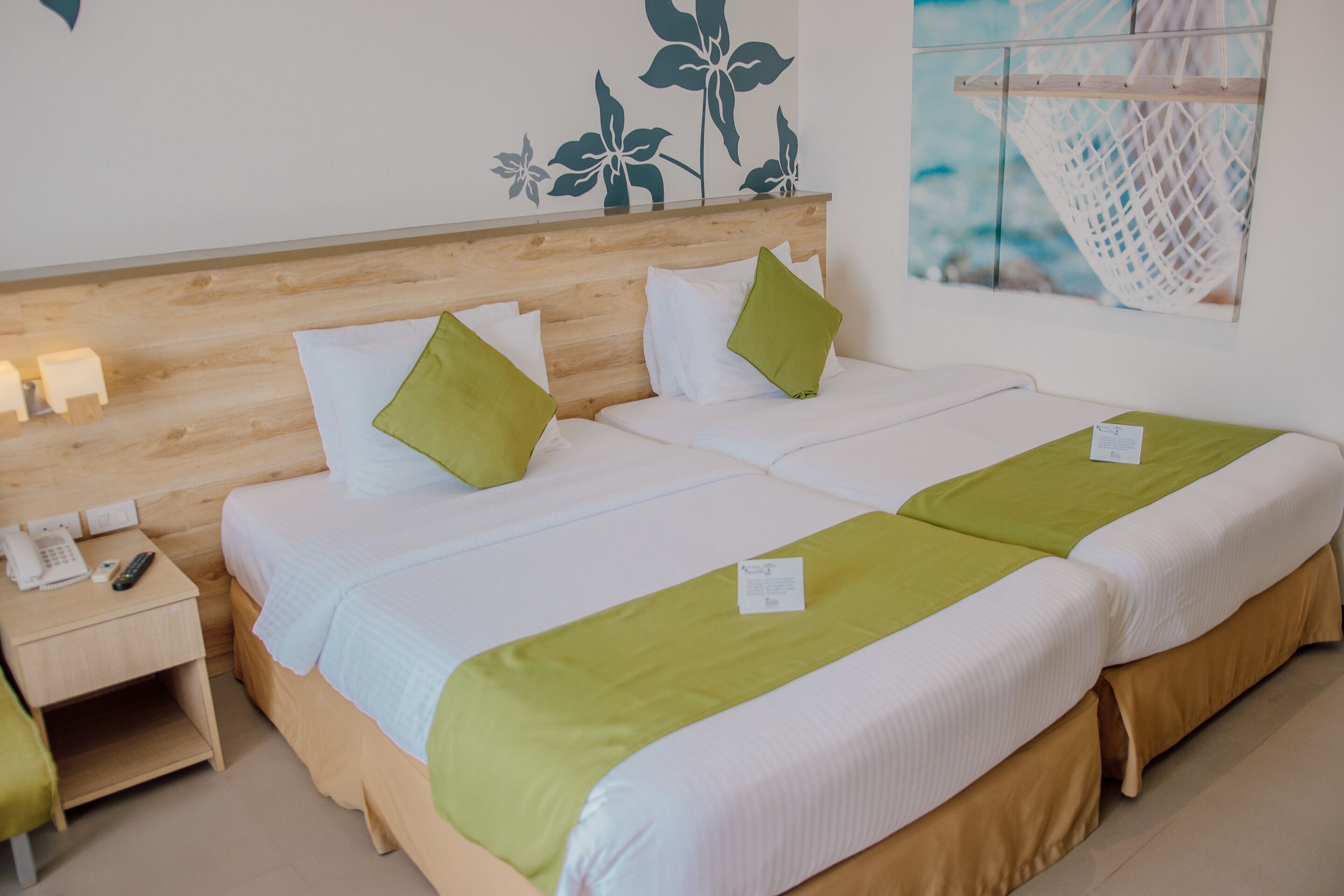 Camera d'albergo con due letti, una testiera in legno, un comodino con il telefono e una parete decorata con un motivo floreale.