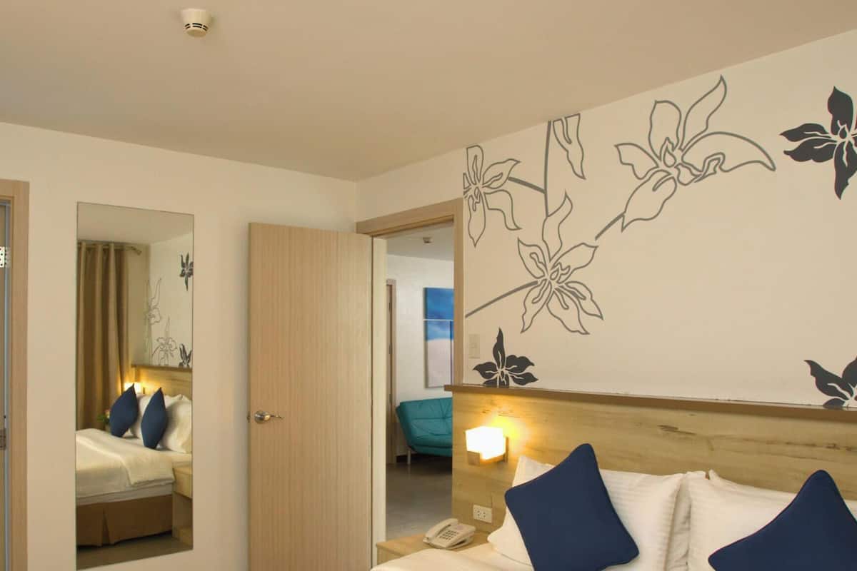 A hotel room with a bed, bedside table, mirror, and a wall with floral wall art.