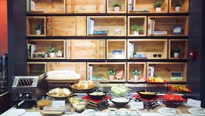A buffet setup with labeled stations for bread, salad, and fruits, surrounded by wooden shelves with books and plants.