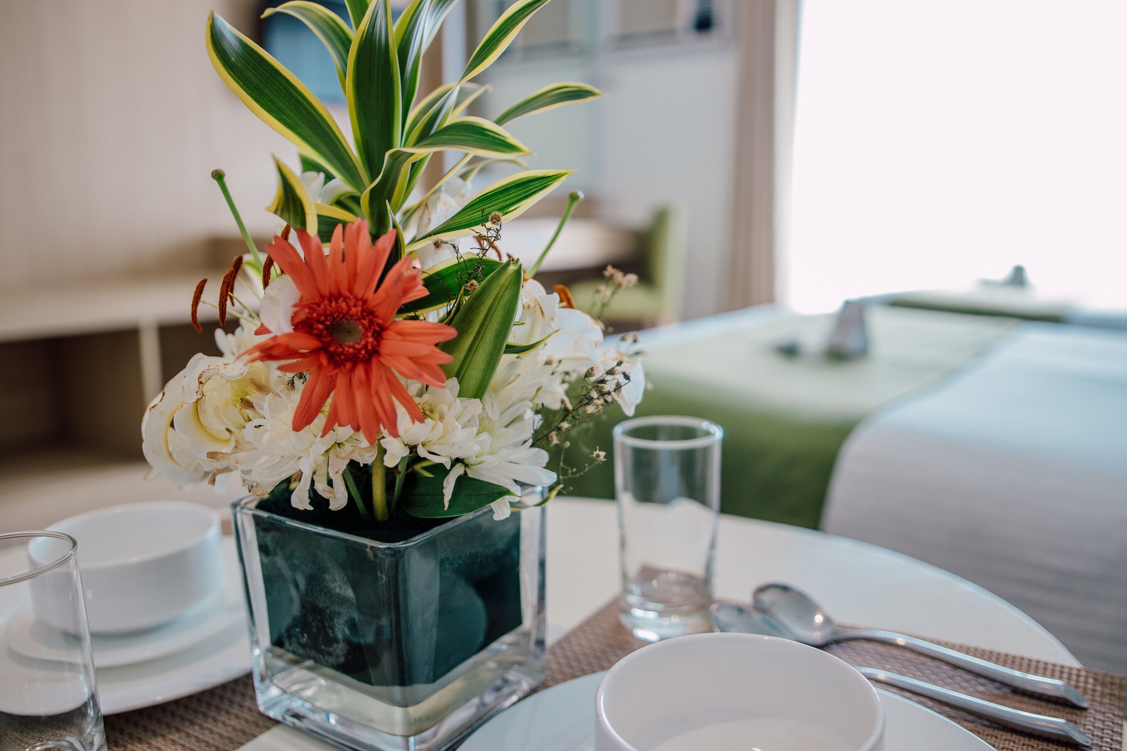 A neatly arranged dining table with a clear glass vase containing flowers, a white plate, a glass, and cutlery.