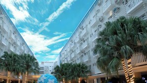 A hotel corridor with multiple floors, palm trees, and a clear sky.