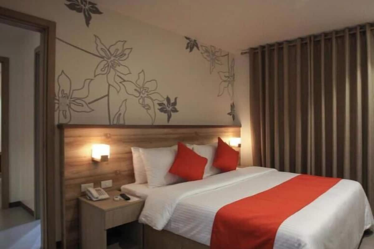 A hotel room with a bed, nightstand, and a wall with floral designs.