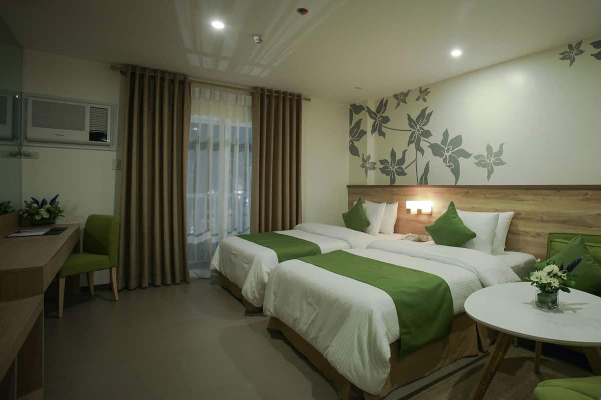 A hotel room with two beds, a desk, a chair, a round table, and a window with curtains.