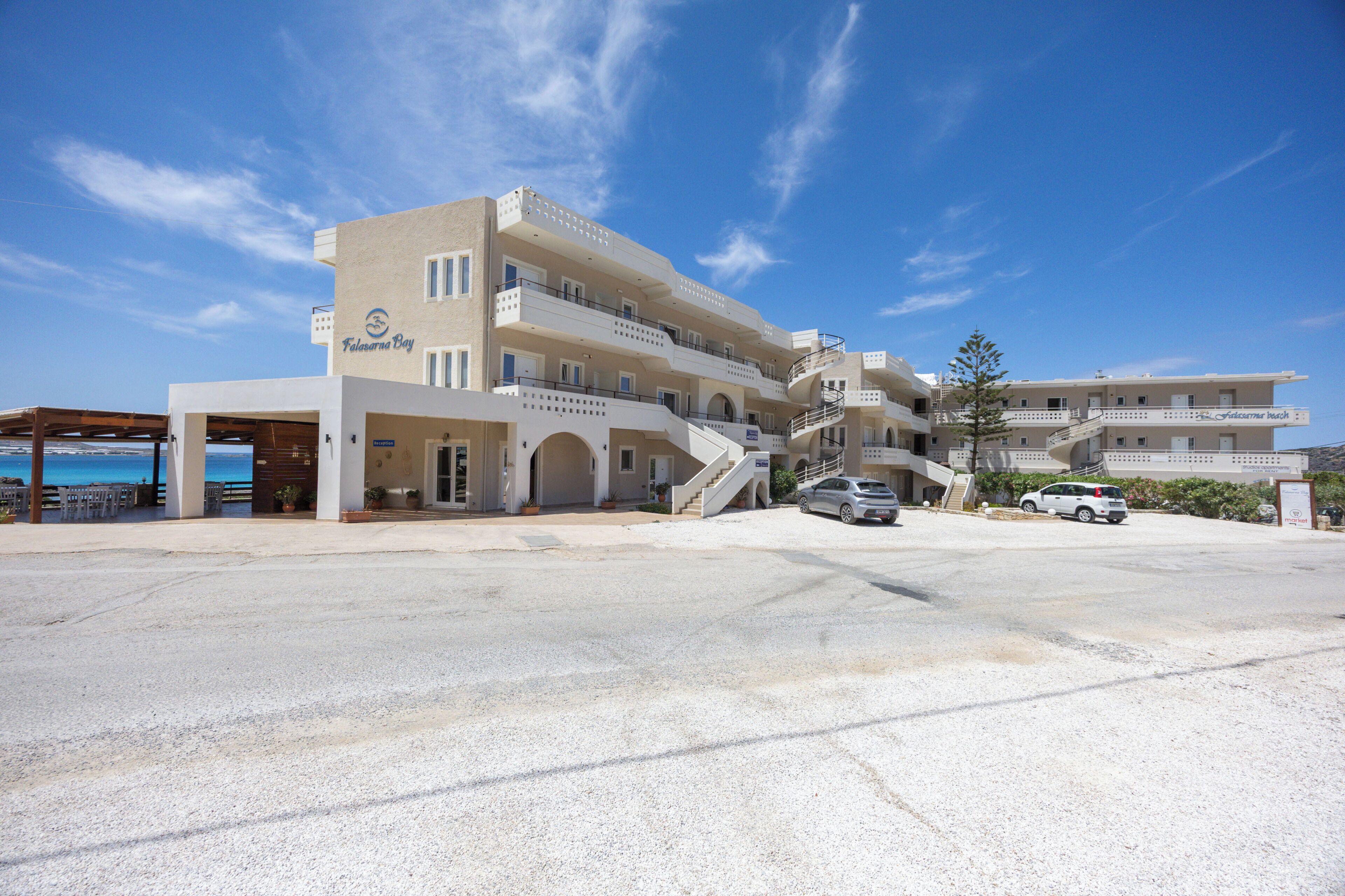 Um hotel com vários andares, uma área externa coberta, uma escadaria que leva à entrada e um estacionamento.