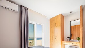 A bedroom with a bed, a wooden wardrobe, a desk with a mirror, and a view of the sea through a sliding door. - Falasarna Bay (Kissamos)