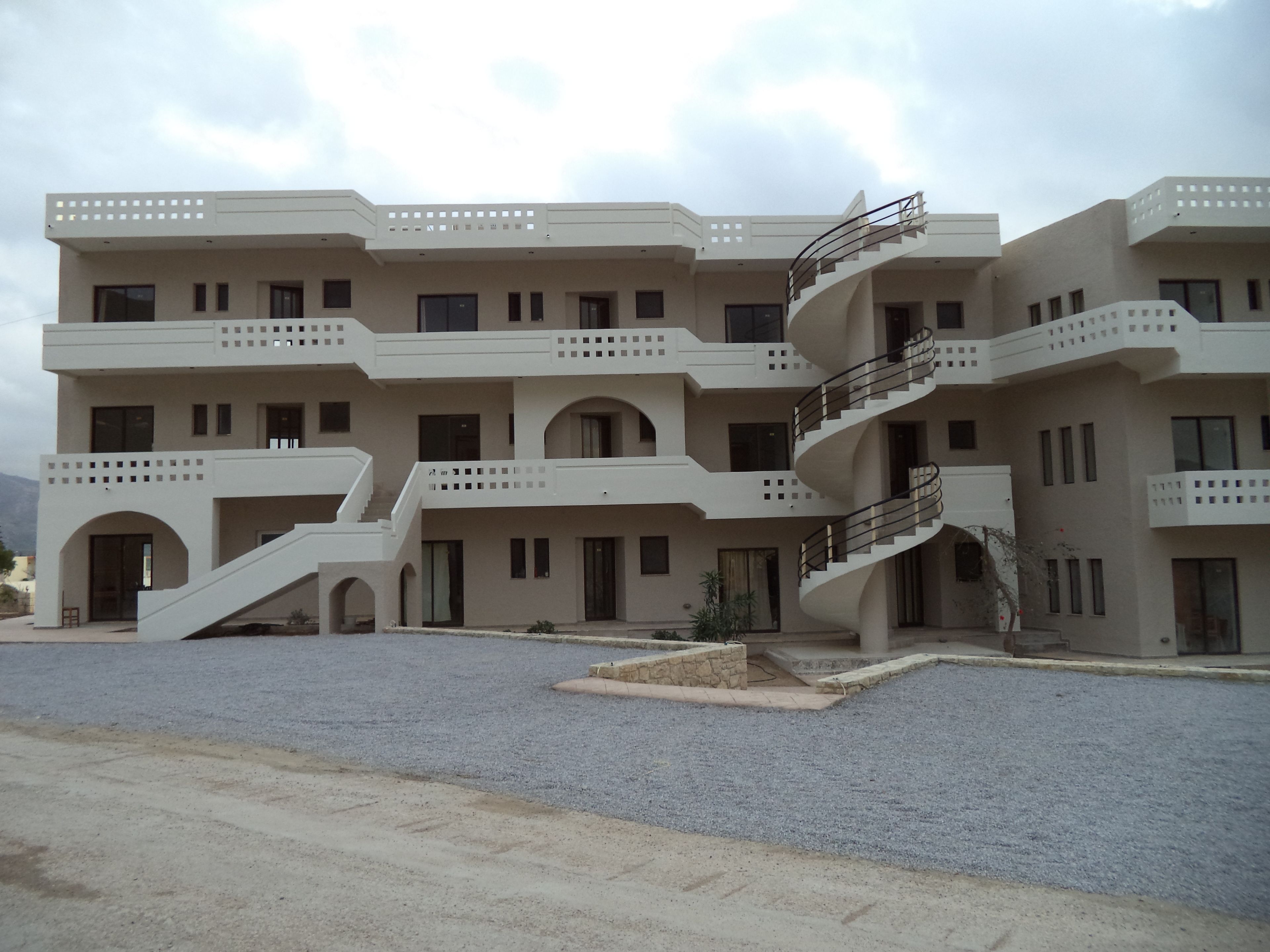 A multi-story building with a central spiral staircase, multiple balconies, and a flat roof.
