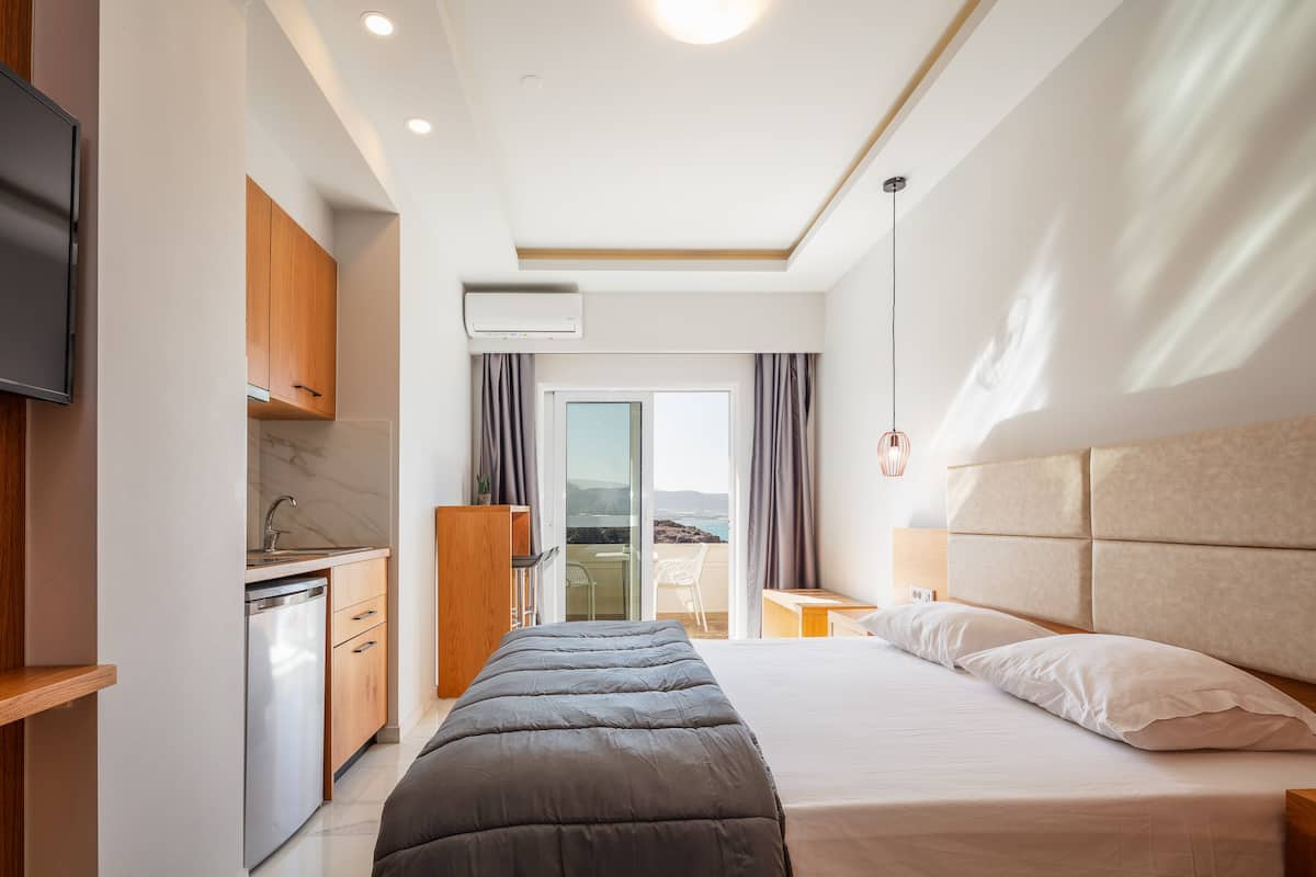 Une chambre d’hôtel moderne équipée d’un lit, d’une petite kitchenette, d’une télévision et offrant une vue sur l’extérieur.