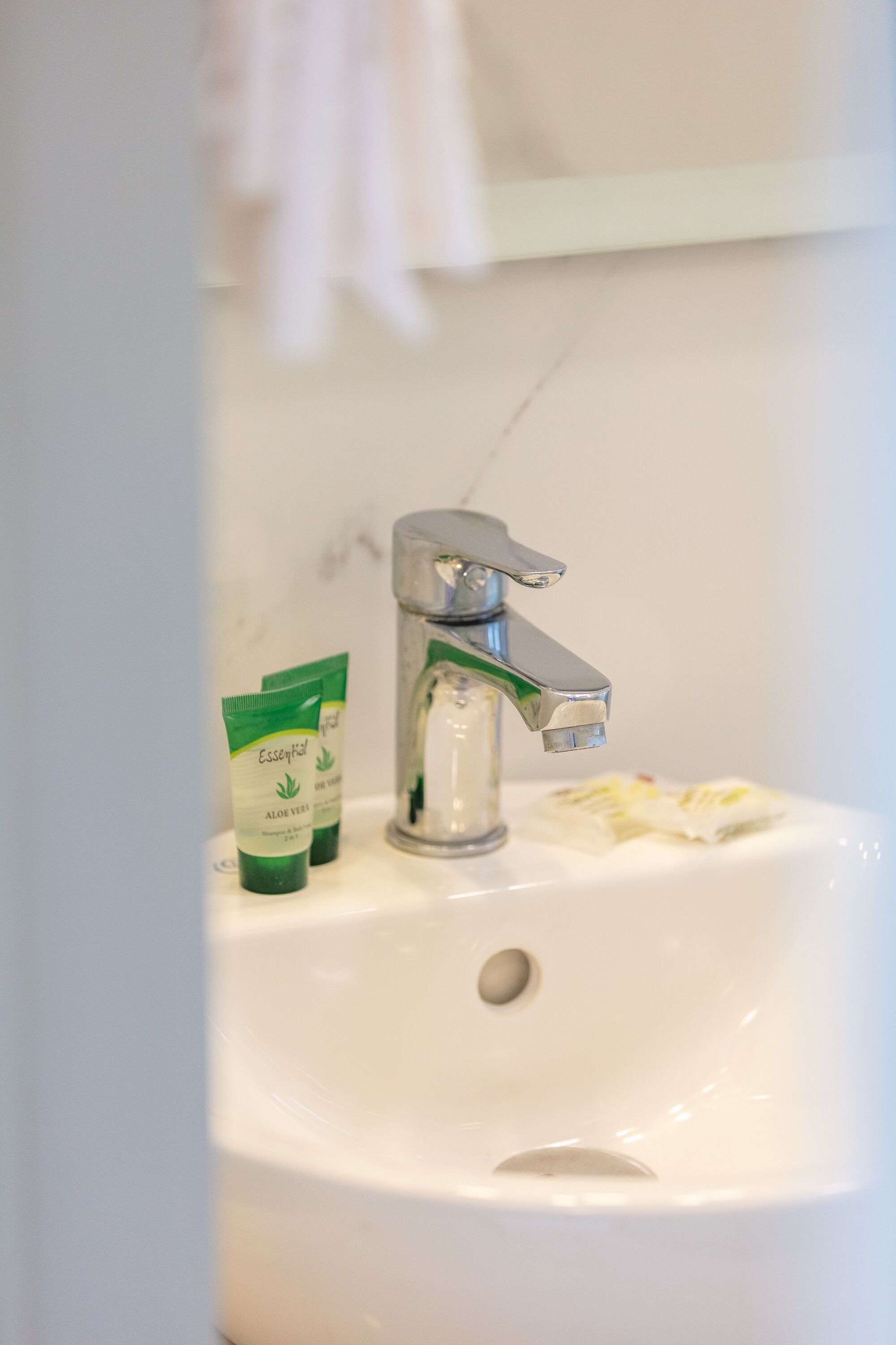 Un lavabo amb un aixeta cromada, dues ampolles verdes etiquetades 'Aloe Vera' i una tovallola blanca penjada a la paret.