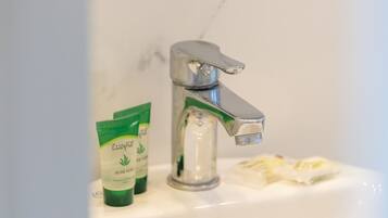 Un lavabo amb un aixeta cromada, dues ampolles verdes etiquetades 'Aloe Vera' i una tovallola blanca penjada a la paret.