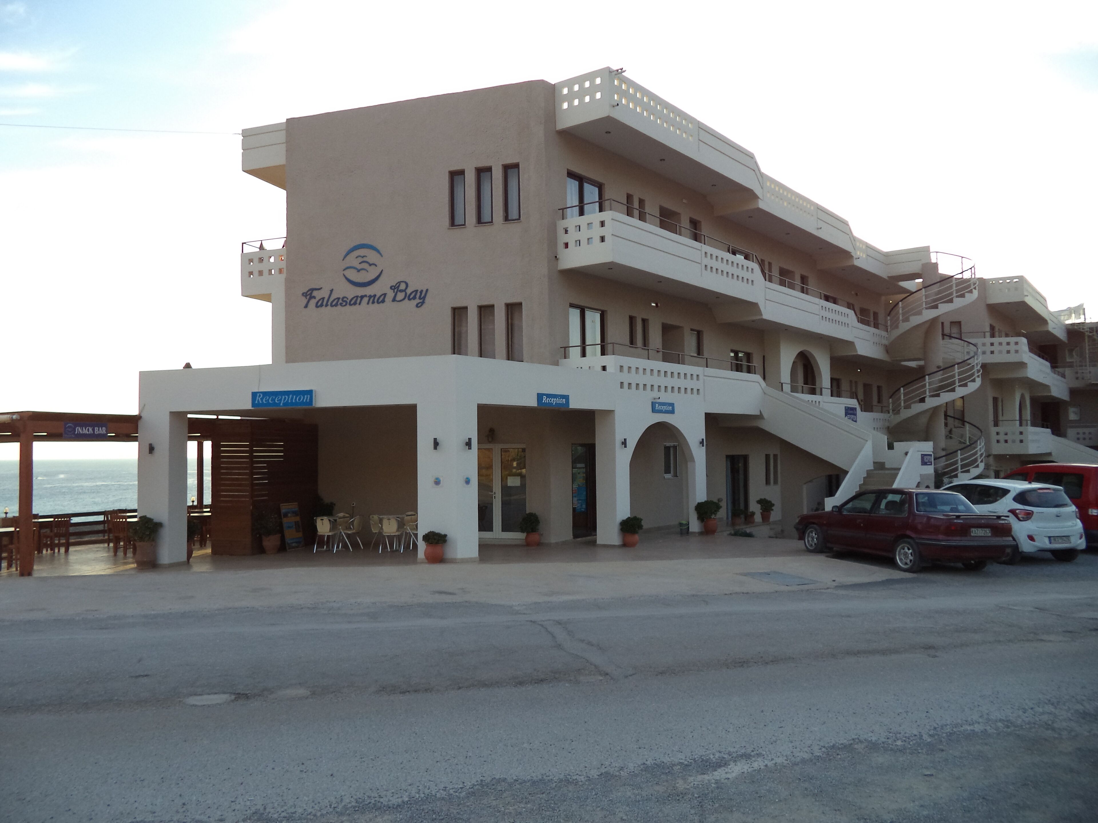A multi-story hotel with a reception area, outdoor seating, and a view of the ocean.
