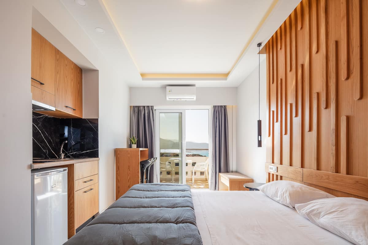 Une chambre d’hôtel moderne équipée d’un lit, d’un petit bureau, d’une armoire intégrée et d’un balcon avec vue.