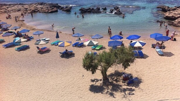 A beach with numerous umbrellas and lounge chairs, rocky formations in the water, and people enjoying the beach. - Falasarna Bay (Kissamos)