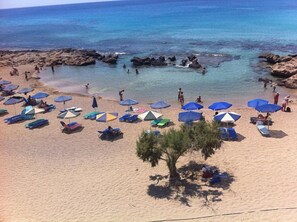 A beach with numerous umbrellas and lounge chairs, rocky formations in the water, and people enjoying the beach. - Falasarna Bay (Kissamos)