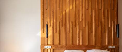 Une chambre à coucher avec une tête de lit en bois, un lit recouvert d’une literie blanche, une petite table ronde et un luminaire fixé au mur.