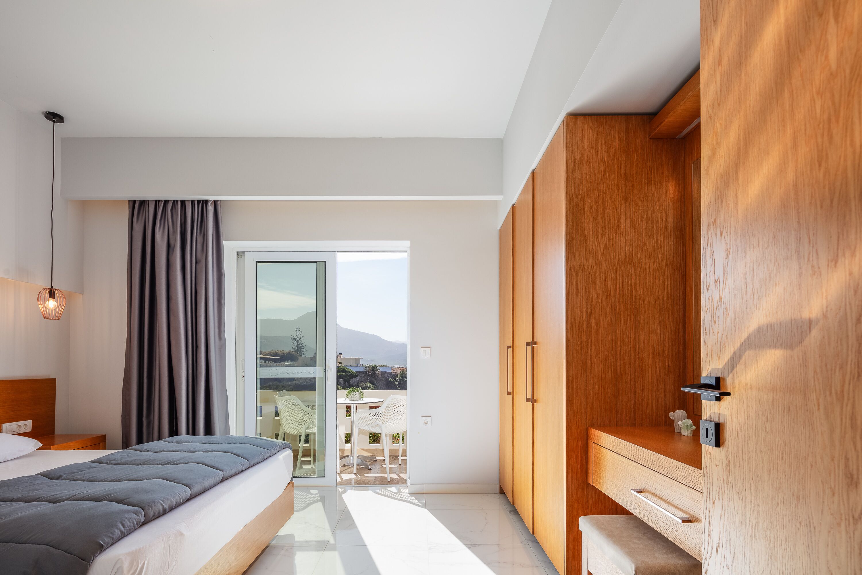 A modern bedroom with a bed, a wooden wardrobe, a desk, and a balcony with a view.