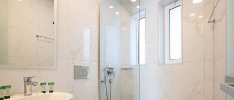 Un baño moderno con un lavamanos grande de color blanco, una ducha con cerramiento de vidrio y un espejo sobre el lavamanos.