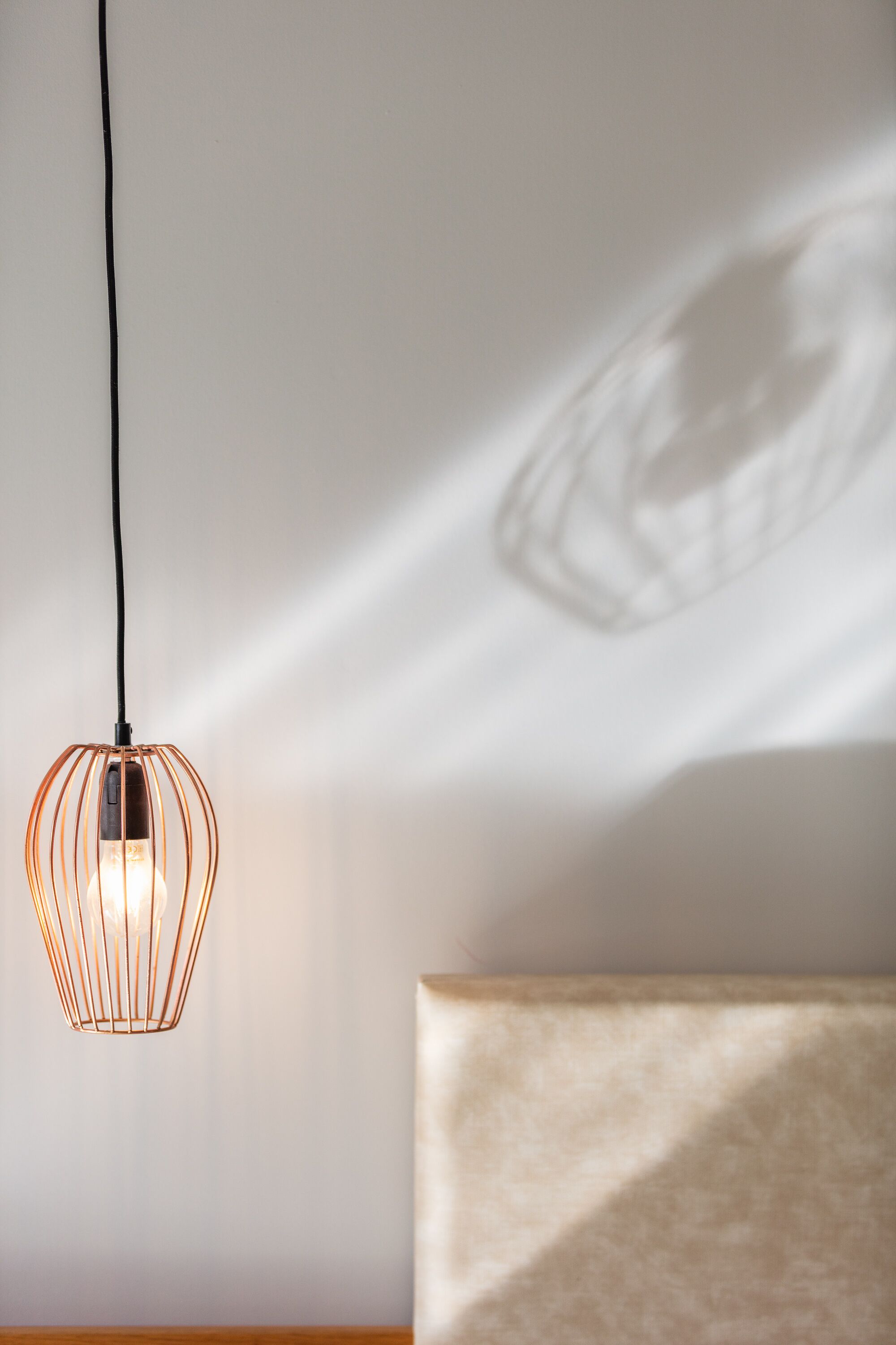 A hanging light fixture with a geometric design, a shadow on the wall, and a piece of furniture with a textured surface.