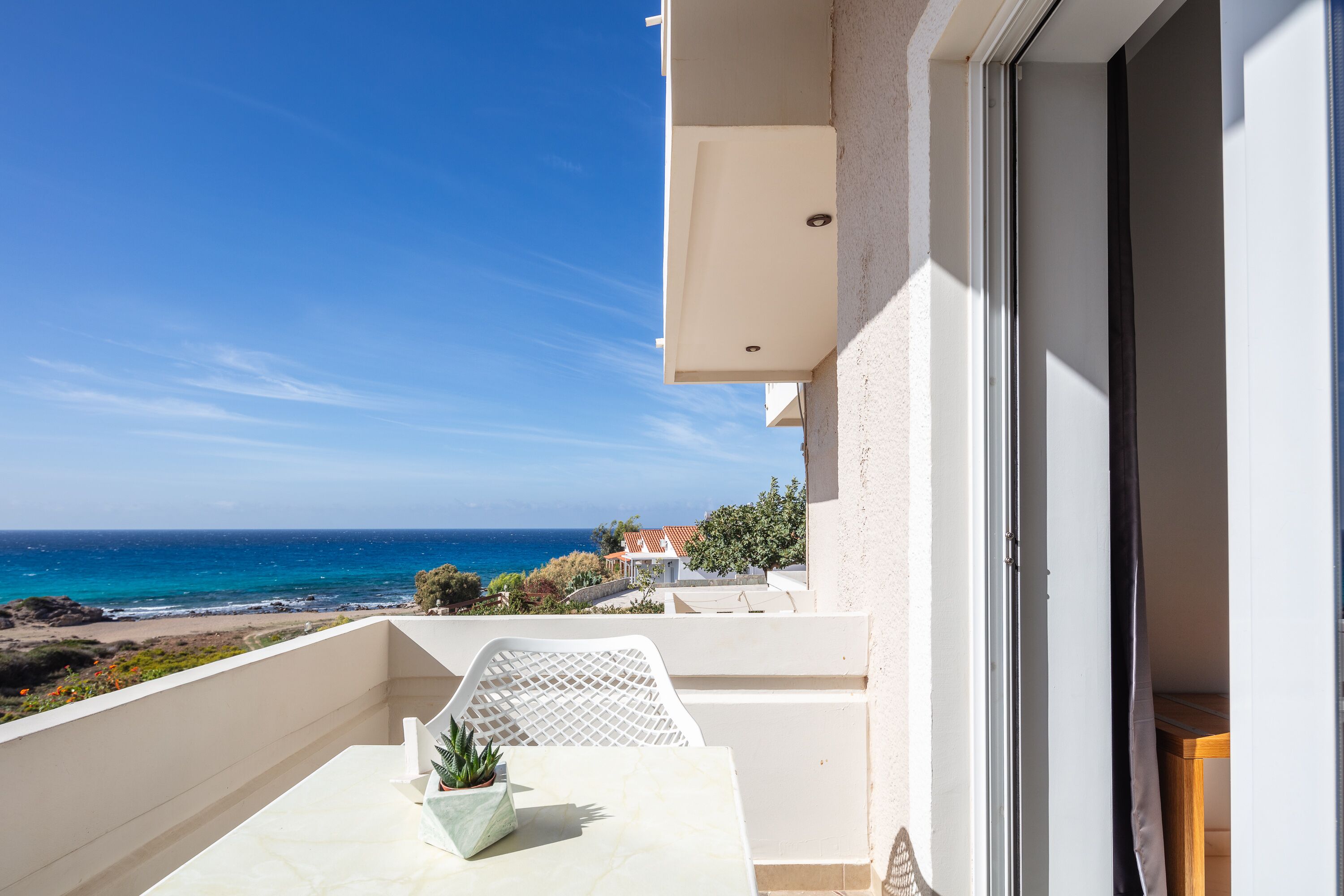 A balcony with a view of the sea, a potted plant, and a door to the right.