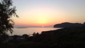 Solnedgang ud over kysten med silhuetten af en klippe og sparsom vegetation.