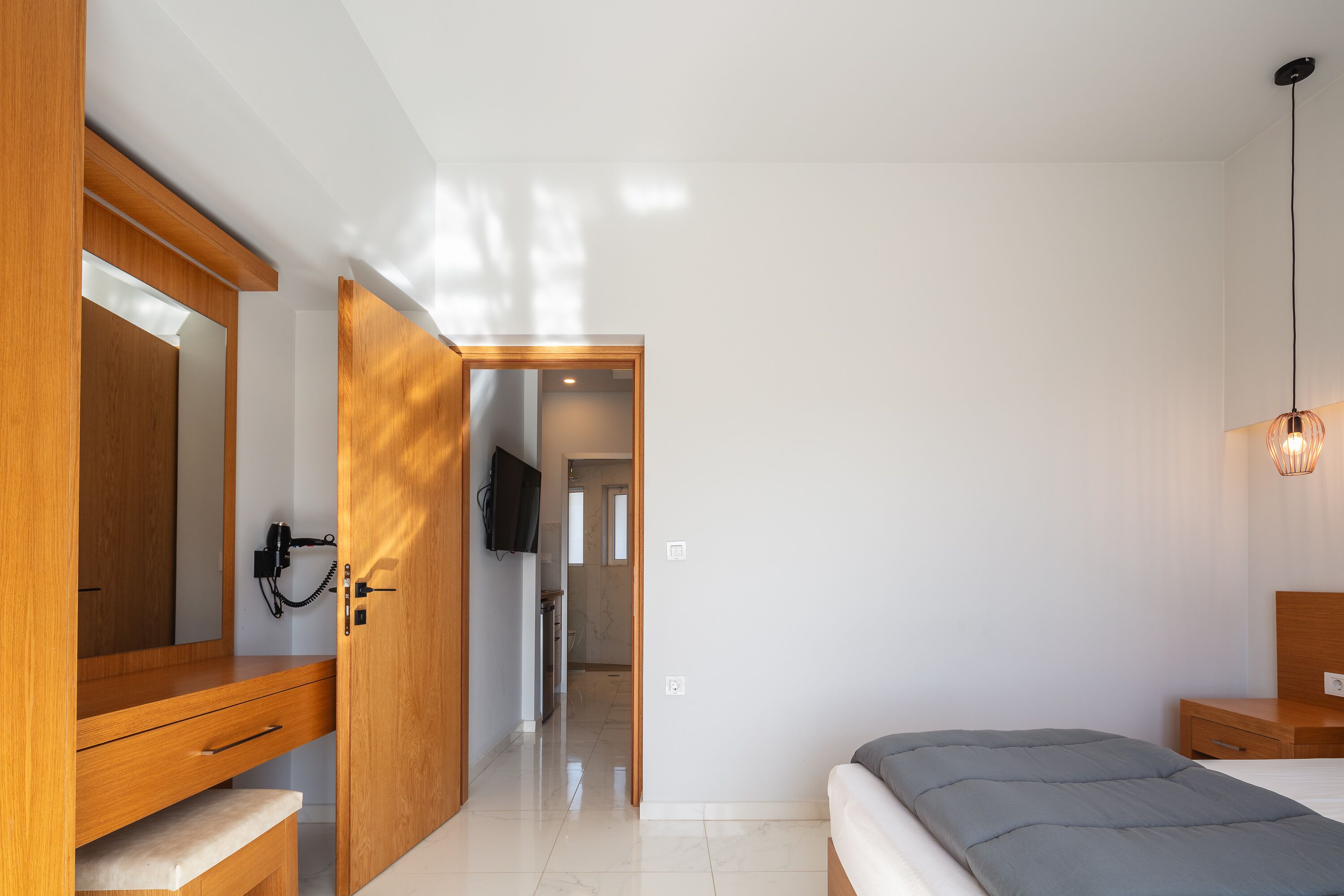 Un dormitorio moderno con un armario de madera, una mesita de noche, una cama con colchón gris y una lámpara colgante.