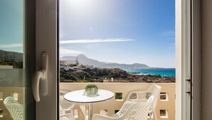 A balcony with a white table and chairs, overlooking a coastal landscape with mountains and the sea. - Falasarna Bay (Kissamos)