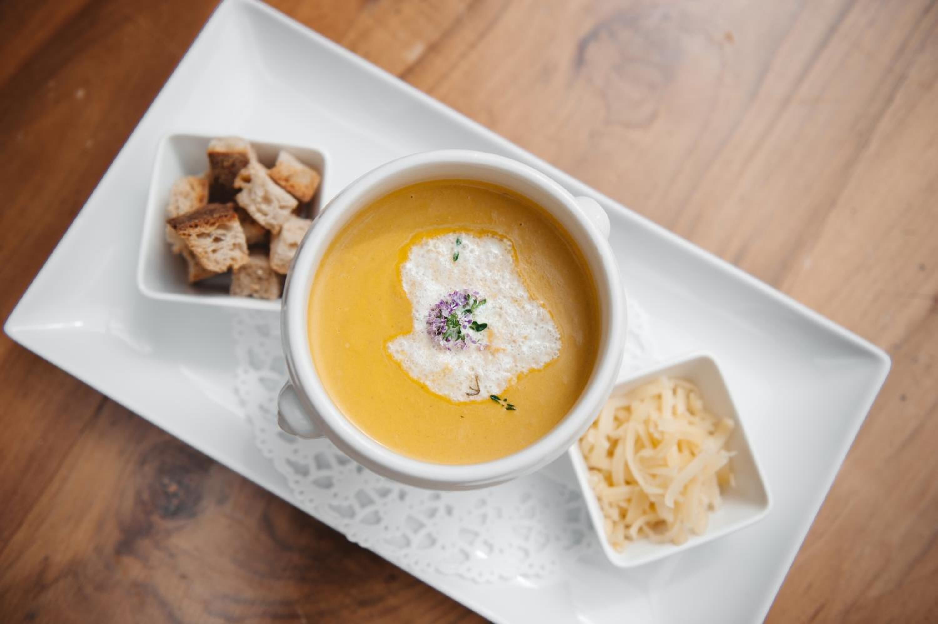 Un tazón de crema de sopa con crutones y queso rallado sobre un plato blanco.