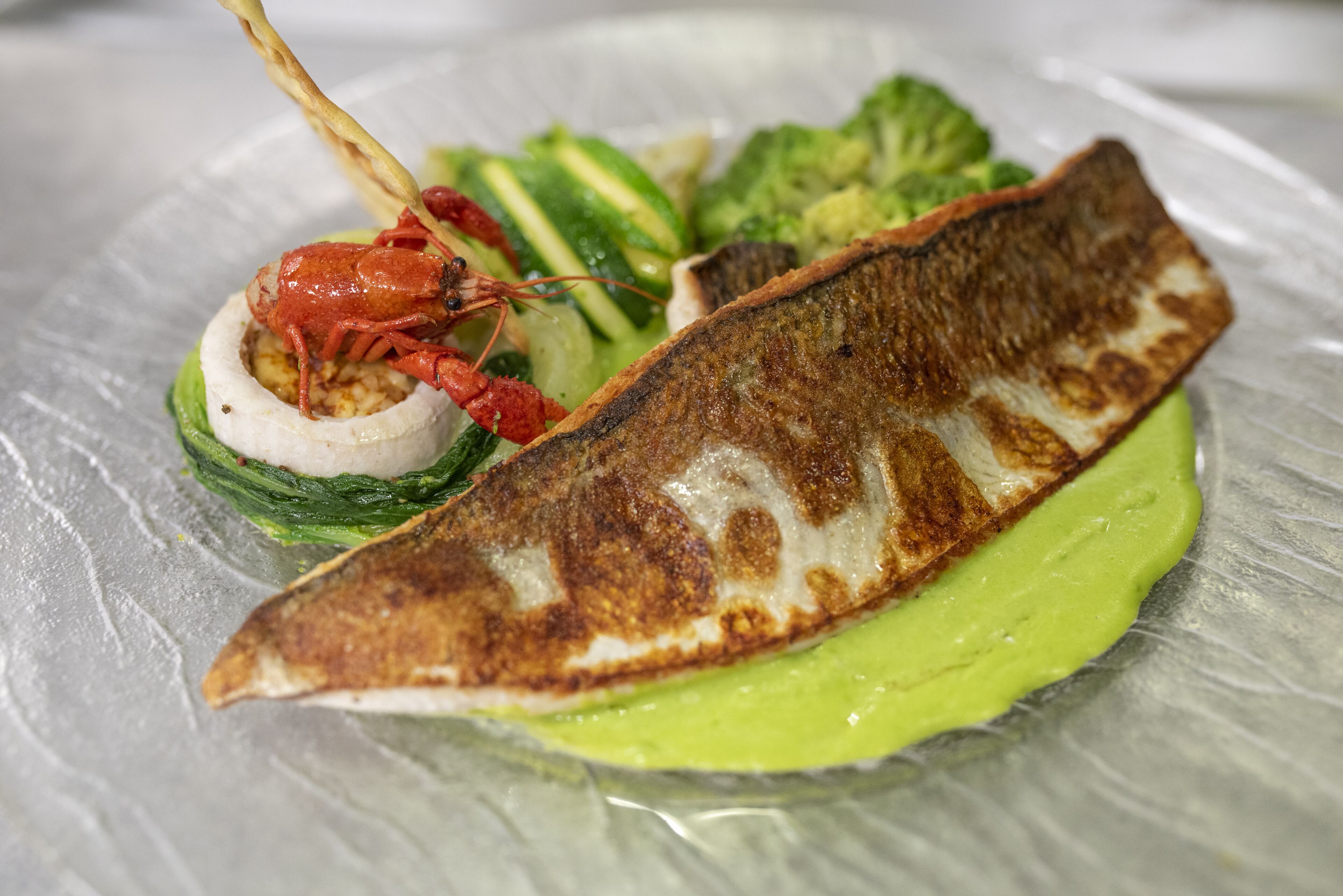 Un plato con pescado a la parrilla, verduras y una cola de langosta.
