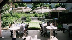 An outdoor patio with tables and chairs, covered by umbrellas, and a view of a garden and mountains. - Auberge d'Anthy (Anthy-sur-Leman)