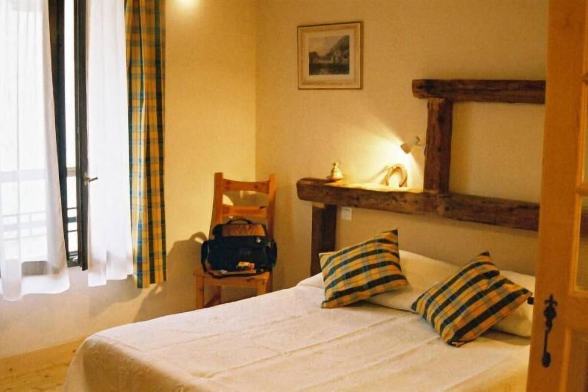 A bedroom with a bed, pillows, a chair, a wooden shelf, and a painting on the wall.