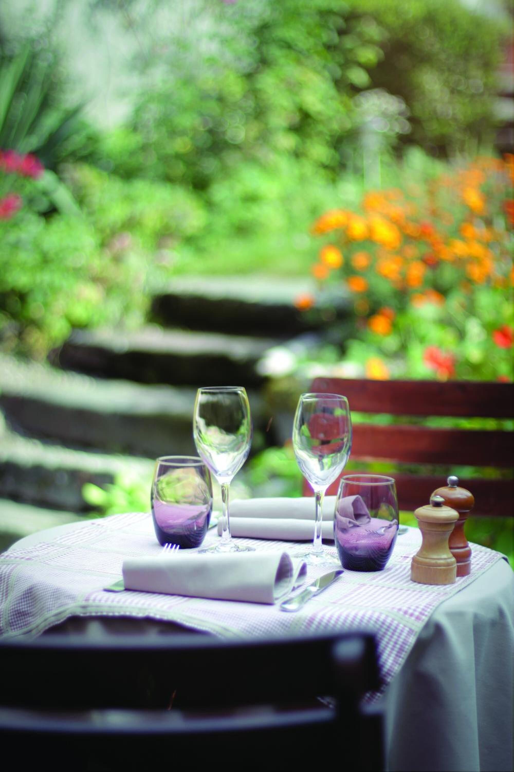A table set outdoors with wine glasses, a salt shaker, and a pepper shaker on a tablecloth.