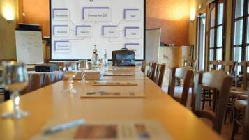 Ein Konferenzraum mit einem langen Tisch, Stühlen, einer Projektionsleinwand, die eine Präsentation zeigt, und einer Tafel im Hintergrund.