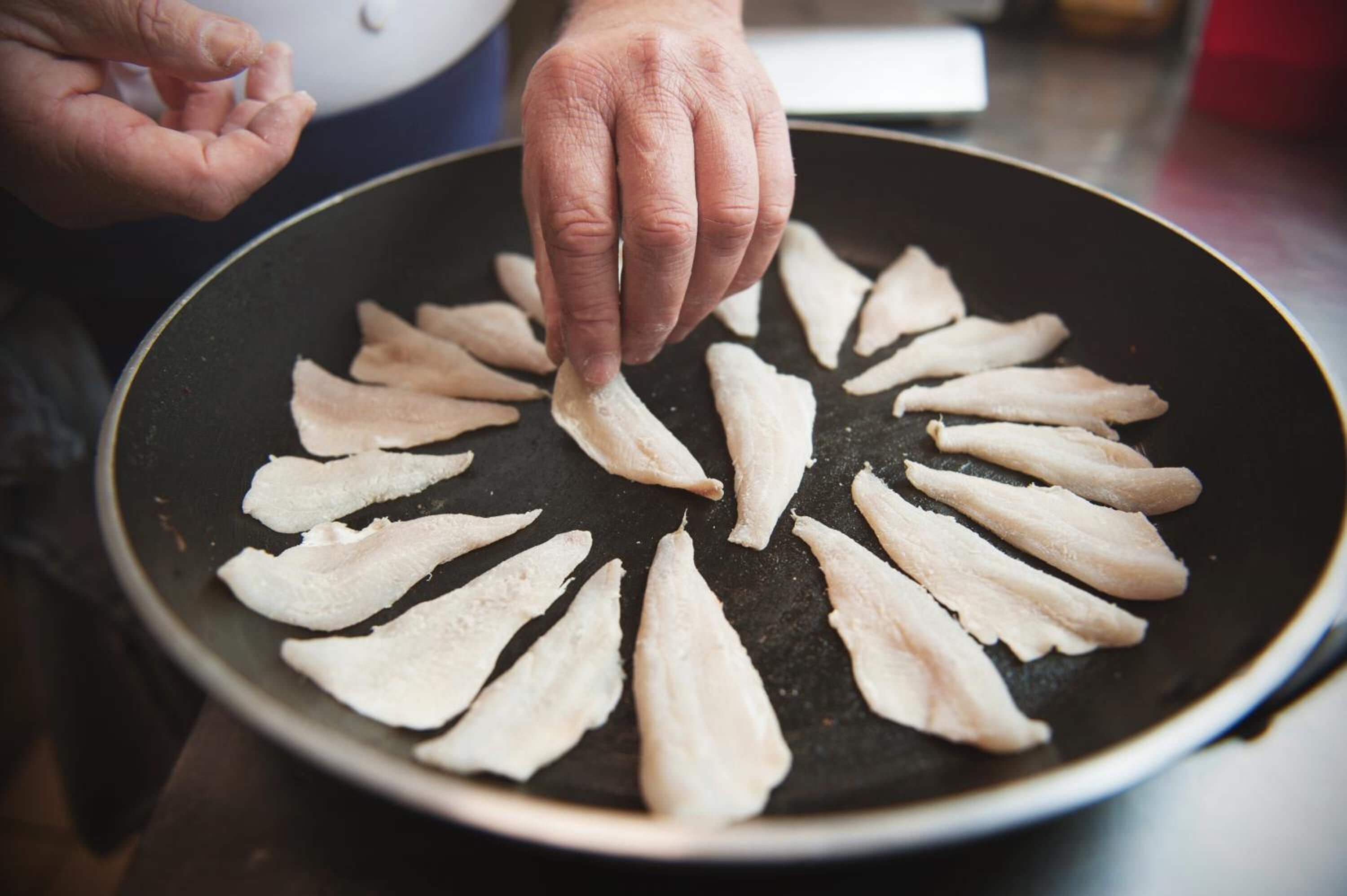 Une personne dispose des morceaux de nourriture, fins et plats, en cercle sur une plaque de cuisson.