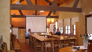A rustic dining area with wooden tables and chairs, a projector screen, and a large window. - Auberge d'Anthy (Anthy-sur-Leman)