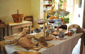 A table with various food items and bread, including baguettes and a tiered stand with bowls and jars.