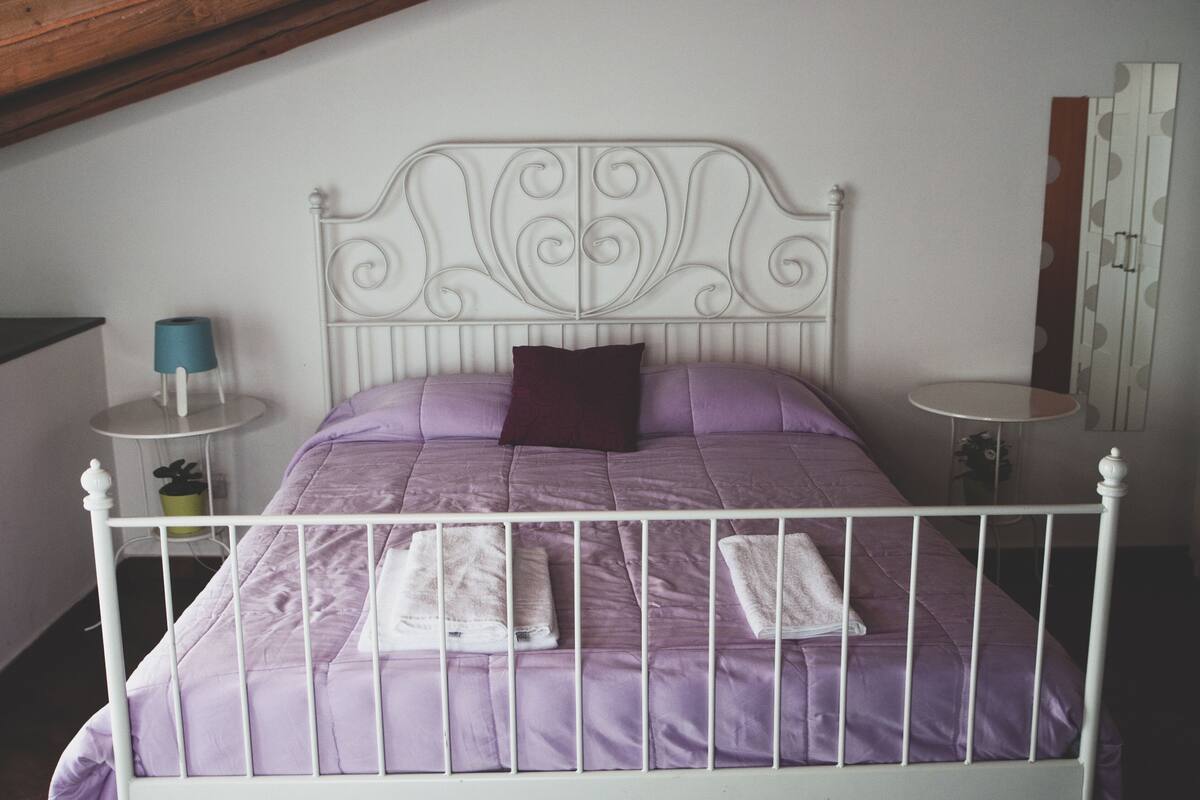 Un lit avec un cadre en métal blanc, une literie violette et deux serviettes blanches.